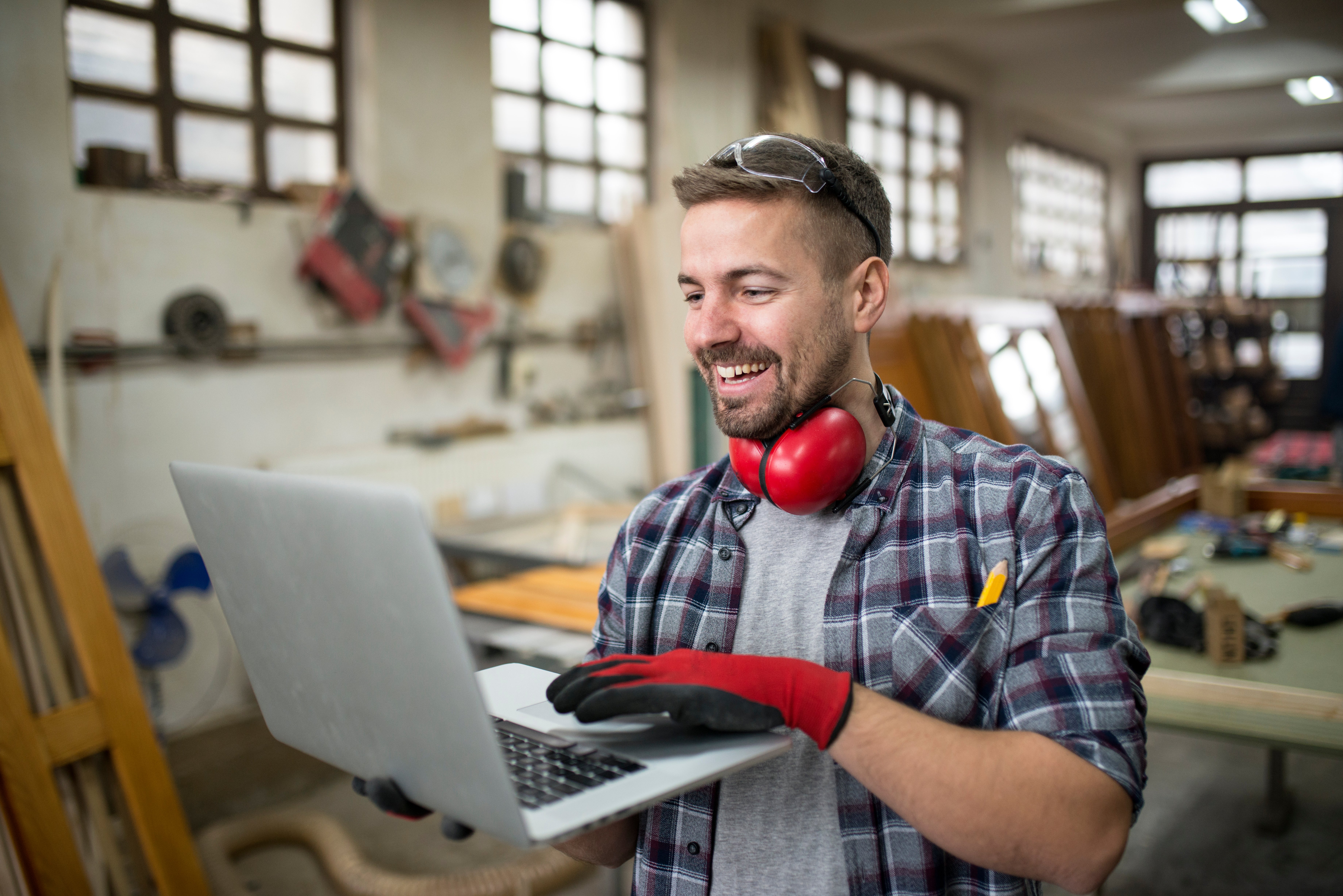 smiling-positive-carpenter-using-laptop-computer-carpentry-workshop-sharing-ideas